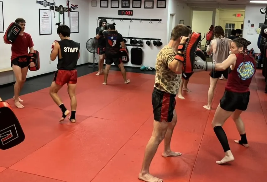 Adult students drilling kicks and punches on pads in a Texas Muay Thai class