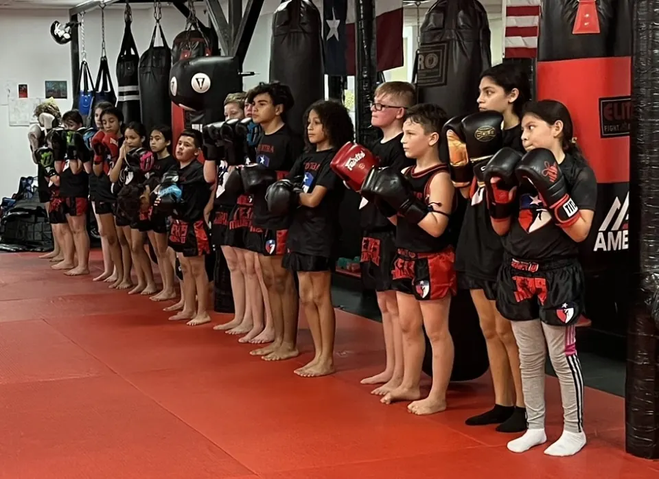 Kids in Texas Muay Thai shirts lined up with their gloves on